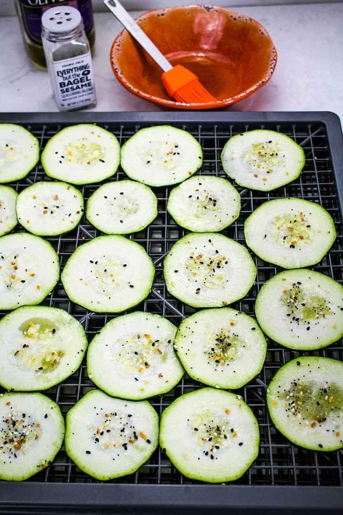 zucchini slices on dehydrator tray with seasoning sprinkled on top