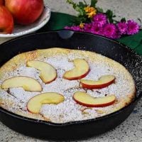 Apple Dutch Baby topped with fresh apple slices and whole apples in the background
