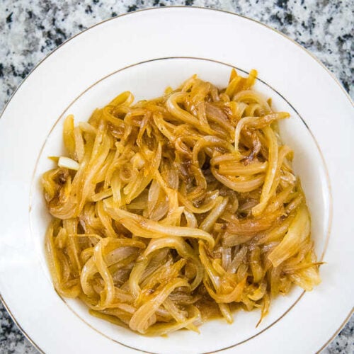 Overhead view of golden caramelized onions in a shallow cream colored bowl with gold trim around the edge and center of the bowl.